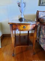 Side table angled showing wood frame, leather top, single drawer with round pull, and lower shelf.