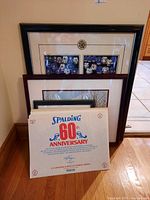 Group of five sports prints, three framed including hockey themes and two unframed sports prints leaning against wall.