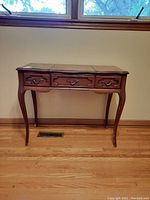 Front view of wooden vanity with three drawers and curved legs