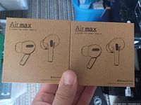 Photo of two unopened Airmax wireless earbuds retail boxes held in hand, showing front packaging with earbuds illustrations and brand name.