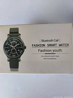 Photo of a smartwatch box showing a black analog-style watch with green strap. Text describes Bluetooth call, fashion smart watch, fashion youth, very attractive watch faces, real time weather.