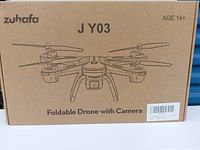 Front of the packaging box showing brand Zuhafa, model JY03, and product name Foldable Drone with Camera. Recommended age 14+ shown.