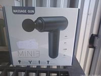 Photo of product box showing image and details of a black mini massage gun with multiple attachment heads.