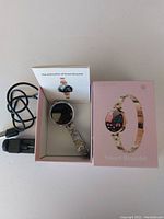 Smart bracelet in its open pink box with charging cable and manual visible