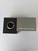 Top view of the sport smart watch in open box with visible silver bezel and black strap next to box lid labeled 'SPORT SMART WATCH'