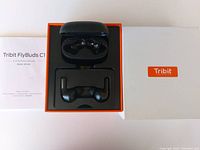 Top view of Tribit Flybuds C1 wireless earbuds inside charging case, with user manual and Tribit box lid displayed.