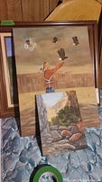 Photo showing three oil paintings: Native American releasing eagles with dreamcatcher, teepee by the river, and canyon landscape with rocks and trees.