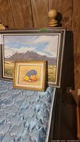Four oil paintings, two visible clearly: arid landscape and fruit still life