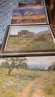 Three framed oil paintings showing rural scenes, including farmhouse, prairie with wildflowers, and western prairie with rocks