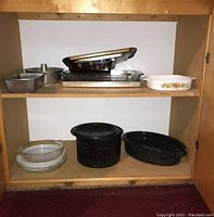 Bakeware items including metal and glass bowls, enamel roasting pan and pot, glass casserole dish, metal baking sheets, loaf pans, and a tube cake pan on shelves.