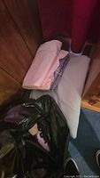 Photo showing folded pink and purple sheets or pillowcases and a white full size comforter; items partially covered with black trash bag.