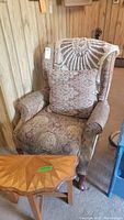 Wingback chair with floral patterned upholstery and decorative cushion, visible in room corner beside wood-paneled wall.