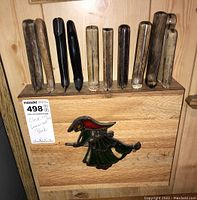 Wooden kitchen knife block containing wooden and black-handled knives with a decorative element on front