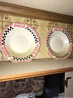 Two Coca-Cola themed plates with red and black checkerboard border and Coca-Cola logos hanging on wall.