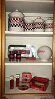 Full shelf showing all Coca-Cola branded items including canisters, salt and pepper shakers, coasters, small tins, and a serving tray.