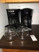 Two coffee makers placed side by side on a dark surface, each with a glass carafe placed in front of them. One is a Mr. Coffee and the other a Black & Decker model.