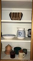 Ceramic taco holder on top shelf and blue and white ceramic pitcher and matching bowl on middle shelf, with various ceramic containers on bottom shelf