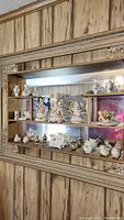 Wide shot showing glass enclosed shelf with multiple shelves filled with Thanes and Chubu hand painted figurines including ceramic birds and boots.