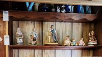 Shelf display with various figurines and dolls including a farmer woman, farmer man, sheriff, small animals, and Santa music box