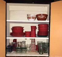 Wide view of cabinet shelves showing bowls, plates, mugs, and glasses arranged in three shelves.
