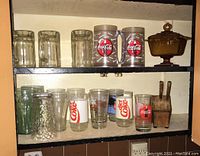 Top shelf containing 3 clear glass mugs, 2 large Coca-Cola plastic mugs, and a brown serving dish with lid