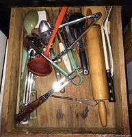 Drawer containing assorted kitchen utensils such as rolling pin, tongs, spoons, forks, whisk, measuring spoons, garlic press, and spatula.