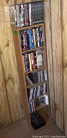 Full view of wooden media shelf in corner with DVDs, CDs, and cassette tapes arranged on shelves.