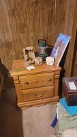 Photo showing wooden nightstand with various items on top including crystal candlestick, owl sculptures, lantern and unicorn painting leaning against the wall.