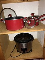 Photo showing three red pots with lids and the bottom shelf with a stainless steel slow cooker.