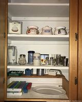 Photo of cabinet shelves showing pill organizers, soup bowls with decorative fruit illustrations, small glass jars, a measuring cup, and a garlic roaster.