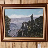 Framed mountain landscape painting with rocky formations beneath a blue sky