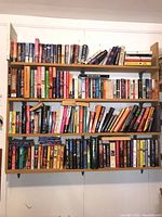 Bookshelves filled with assorted hardcover and paperback books, arranged side by side and stacked, showing a wide variety of book sizes, covers, and colors