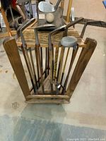 Full view showing multiple antique wooden shaft golf clubs, pool cues inside a solid oak rotating stand.