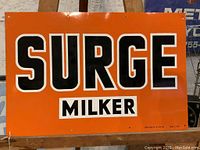 Front view of the orange metal Surge Milker sign with black and white lettering