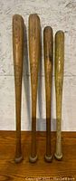 Four wooden vintage baseball bats standing upright, showing general condition and wood grain.