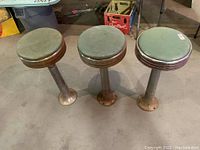Three green vinyl seat stools on metal pedestals, front view