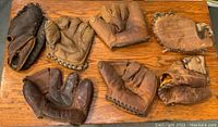Seven vintage baseball mitts laid out on wood table, showing full set included in lot