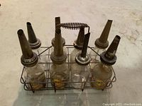 Full view of wire rack with eight glass oil jars and metal spouts