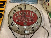 Front view showing convex glass face with Amalie Pennsylvania Motor Oil logo and clock hands
