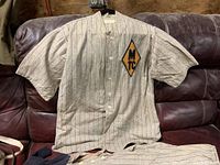 Front view of antique pinstripe baseball shirt with MTC diamond patch, laid on leather couch.