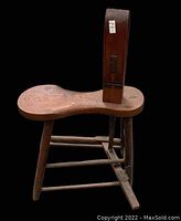 Side view of antique saddle tack bench showing saddle-shaped wooden seat, rectangular backrest, and connecting braces on legs.