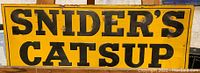 Front view of the rectangular yellow tin tacker sign with large black text reading 'SNIDER'S CATSUP'.
