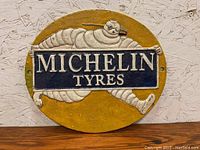 Front view of the oval Michelin Tyres cast iron sign with Michelin Man figure and blue sign in hand.