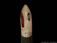 View of folk art painted wooden shell prop top portion showing stylized eye and red geometric pattern.