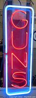 Front view of neon sign light spelling 'GUNS' in red neon with blue neon border.