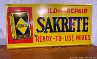 Front of vintage metal Sakrete cement sign showing yellow background with red and black text and graphics.