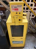 Front view of vintage yellow newspaper dispenser with coin slot and Boston Herald branding.