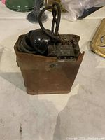 Field telephone inside a brown leather carrying case with black handset resting on top, cords coiled around.