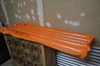 Orange inflatable pool lounger float laid flat showing the full length of the float and its horizontal air tube design.