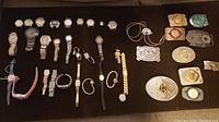 Overhead shot of all wristwatches, belt buckles and bolo cord on black background